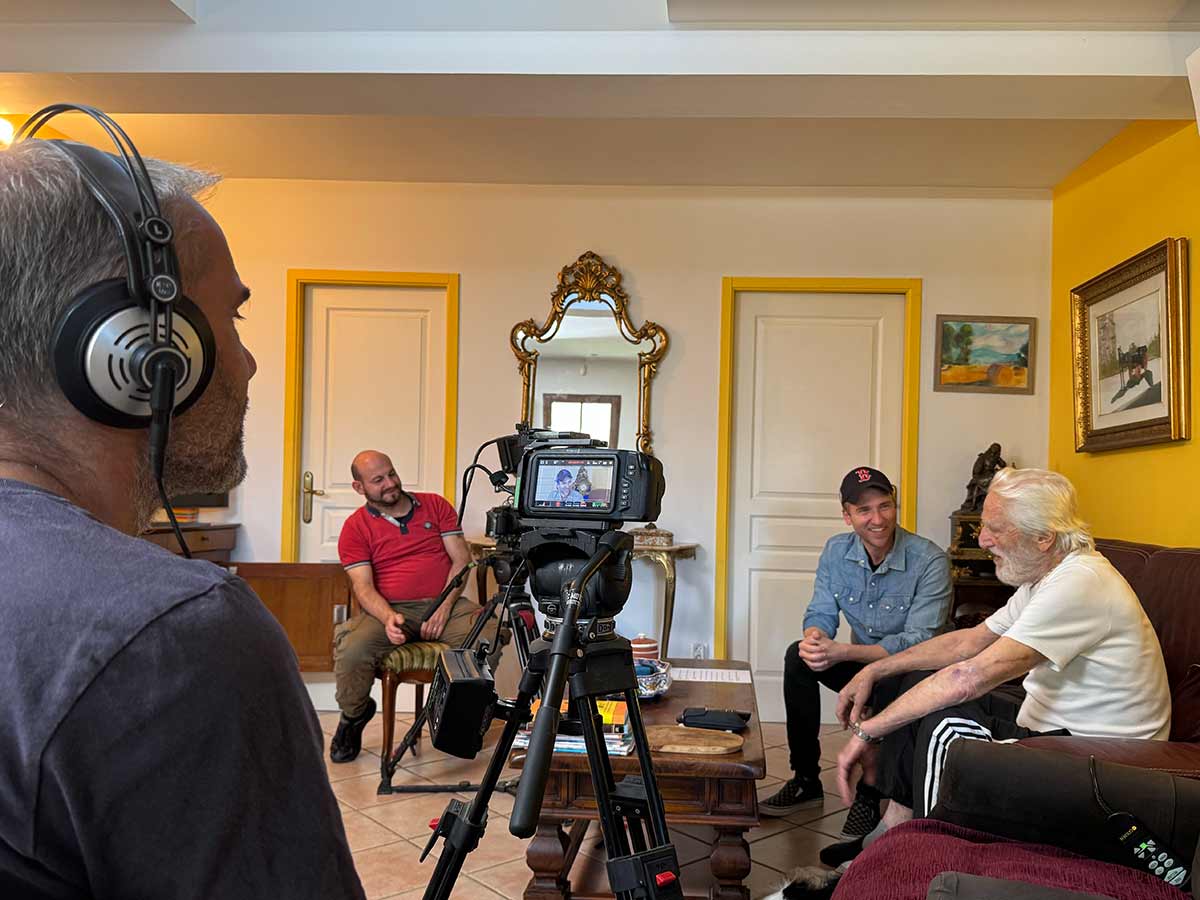 Due uomini davanti ad una videocamera riprendono due uomini seduti su un divano che parlano durante una intervista