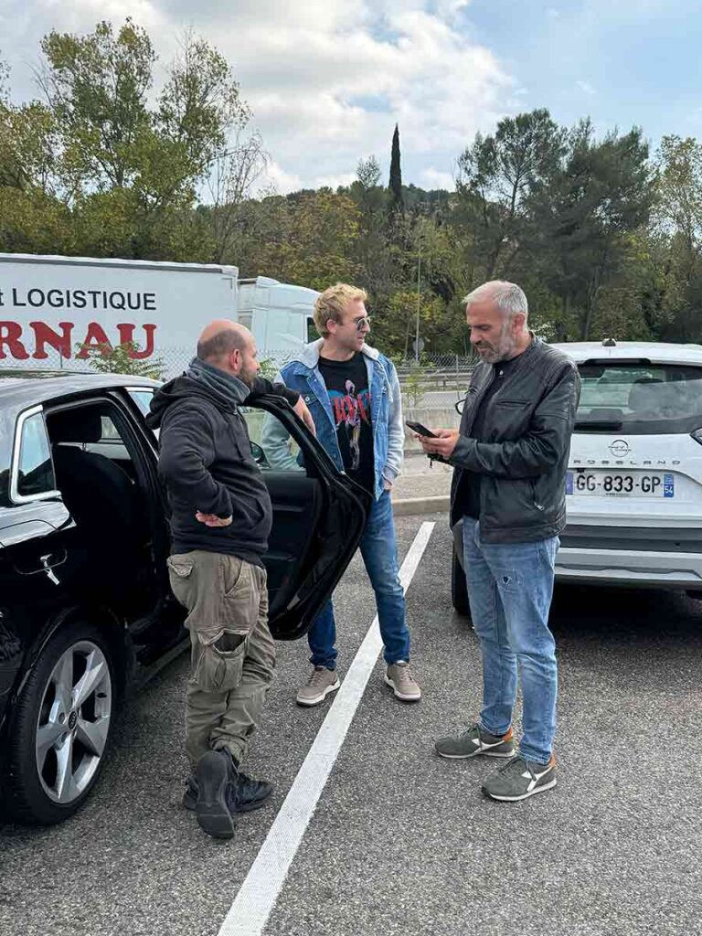 Tre uomini in piedi con accanto ad un'auto parlano su un parcheggio di un'autostrada