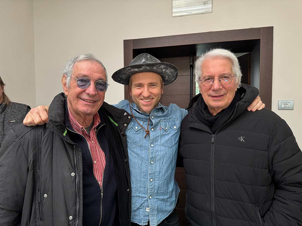 Tre persone in posa sorridono per una foto con alle spalle una porta di ingresso di una stanza