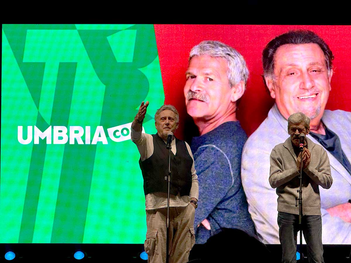 Due attori revitano su un palco con sullo sfondo un grande schermo che proietta la loro immagine